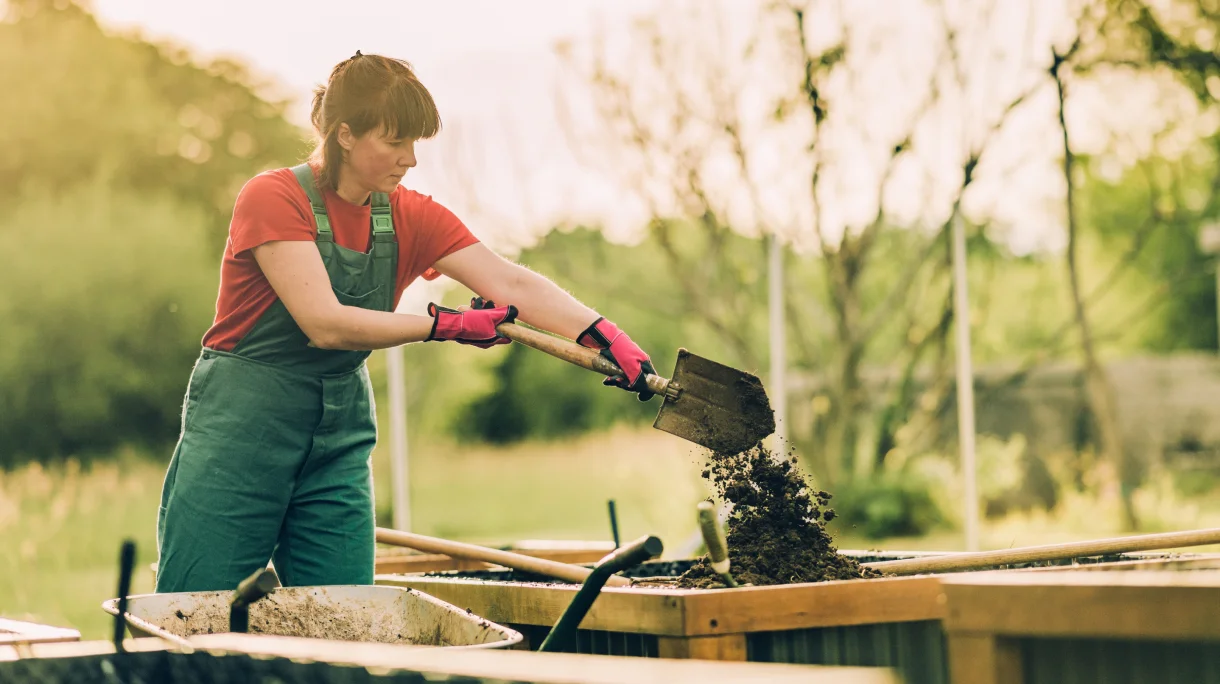Woman adding soil to newly built raised garden bed.