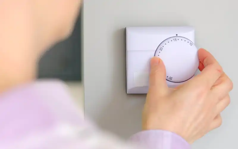 Person adjusting central heating thermostat wheel.