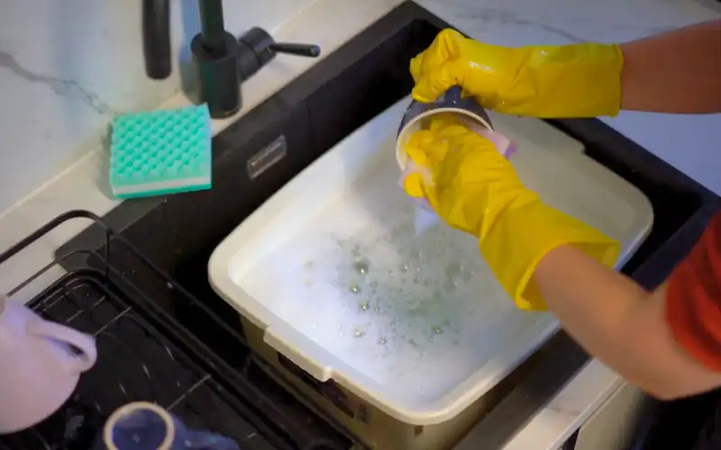 Person washing up at sink with yellow rubber gloves on.
